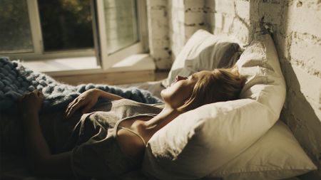 A woman lies in bed asleep next to an open window