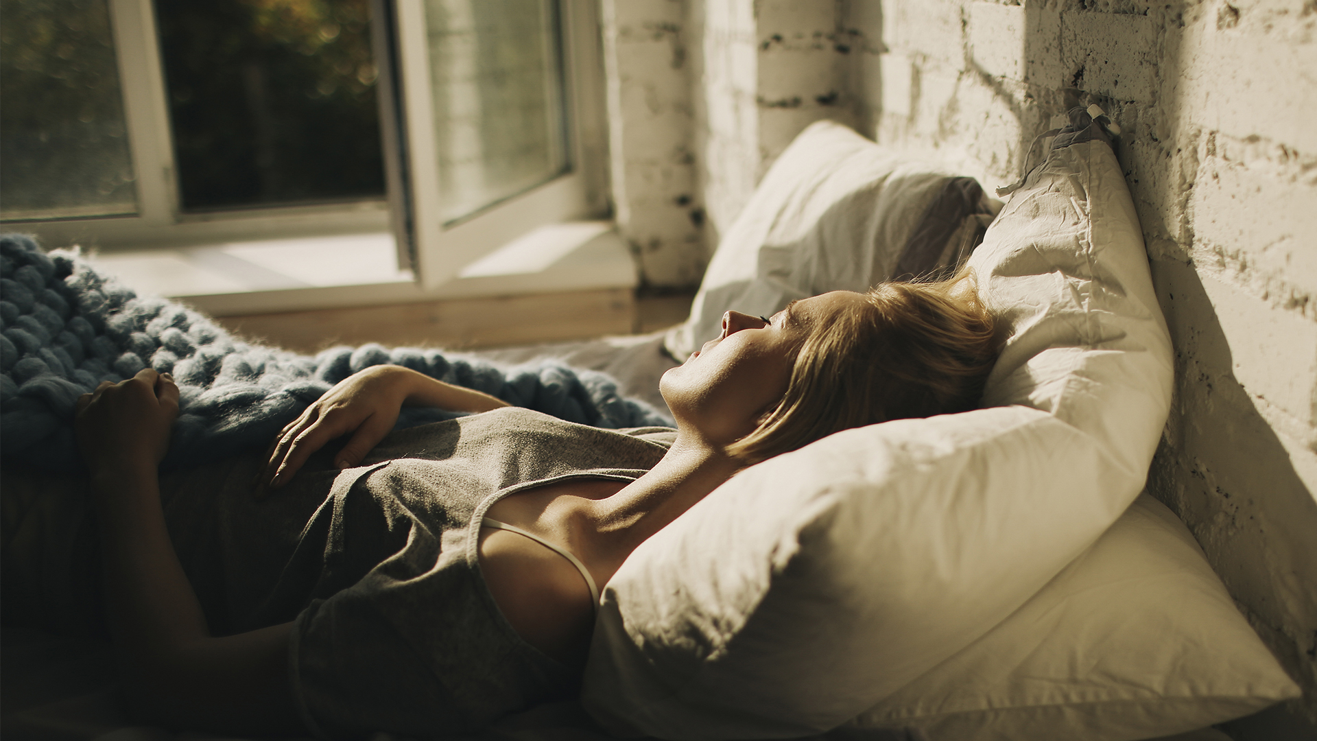 A woman lies in bed asleep next to an open window