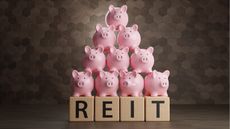 REIT spelled out in wooden blocks with a pyramid of piggy banks on top.