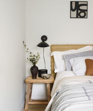 white bedroom with seagrass headboard, wooden stool and black wall light