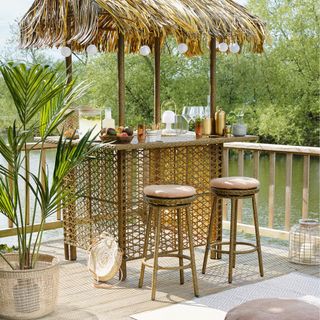 Decking area with wooden railings, straw thatched bar, tiki bar with bar stools and view across a river
