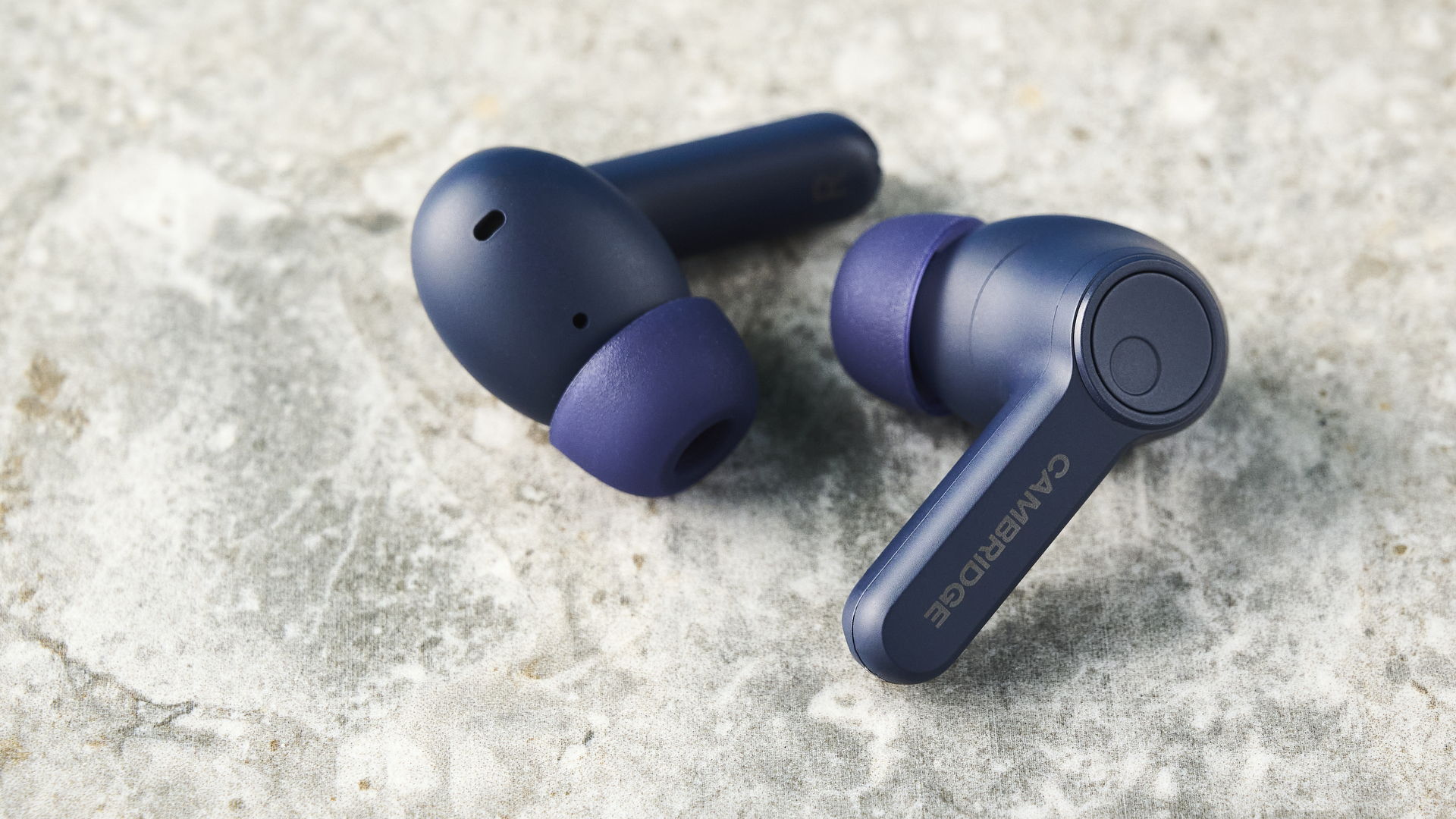 the cambridge audio a100 se earbuds on a blue tom's guide background with a stone-coloured table underneath