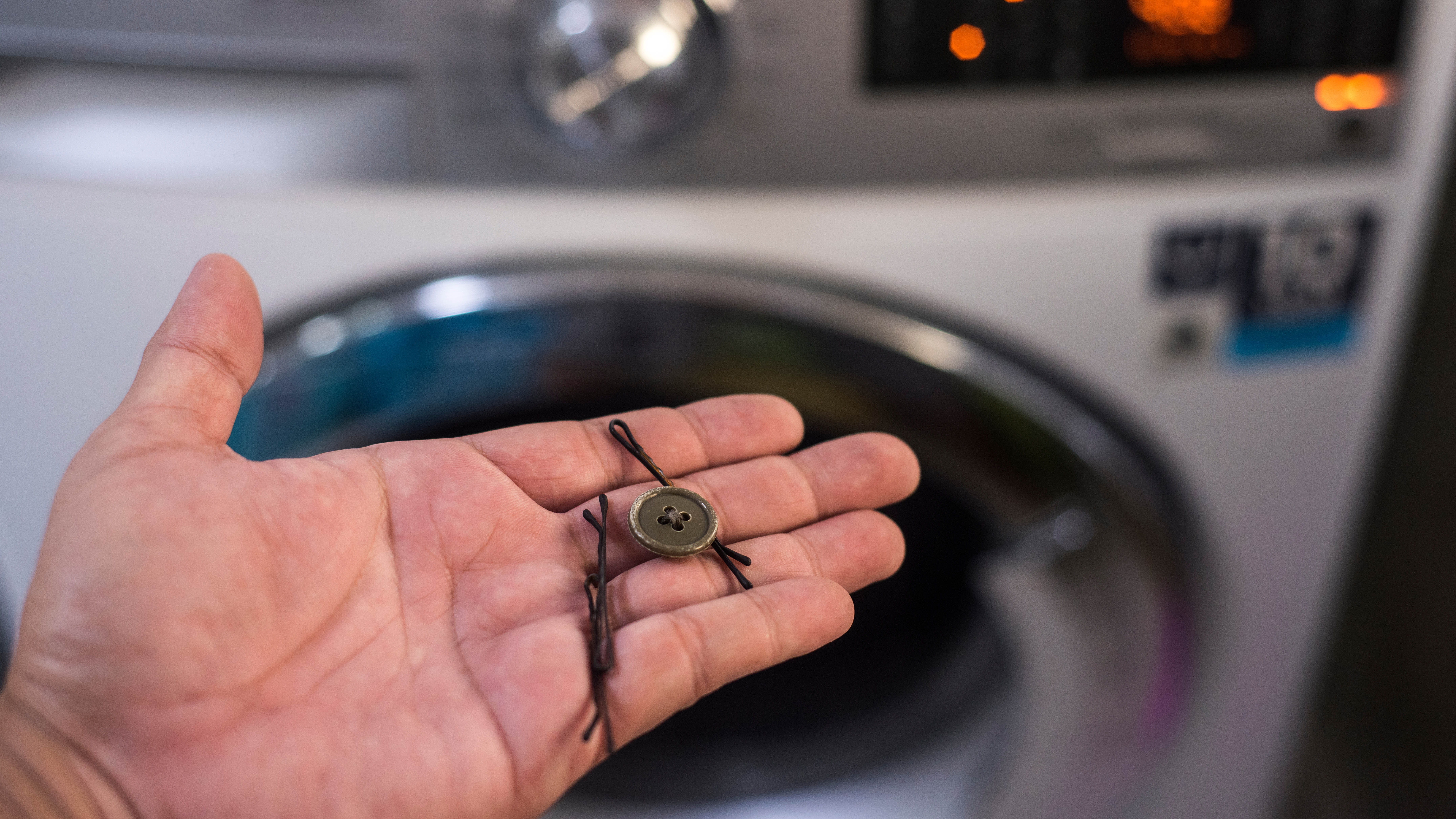 A person holding a hairpin and a button in front of the washing machine