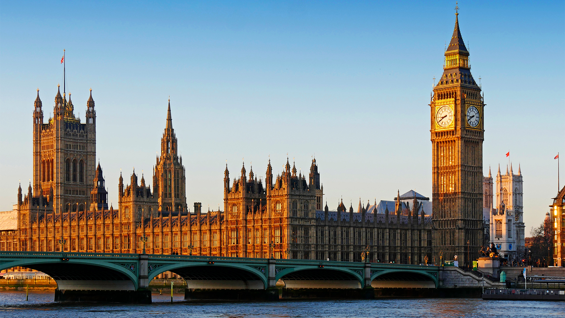 House of Parliament at Westminster pictured at dawn with Big Ben clock tower and Thames River in foreground.