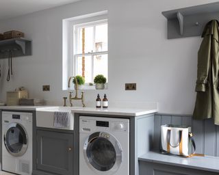 A grey mudroom laundry with washing appliances and bench
