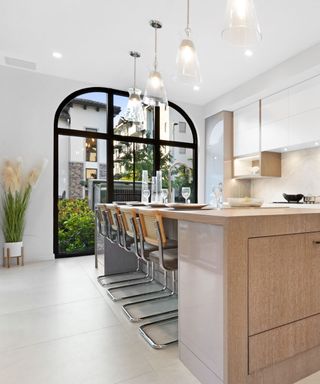 A modern kitchen with wooden cabinetry and an arched glass door with a black frame