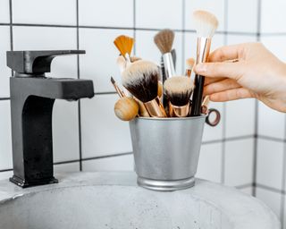 Makeup brushes in silver basket with black tap on the sink