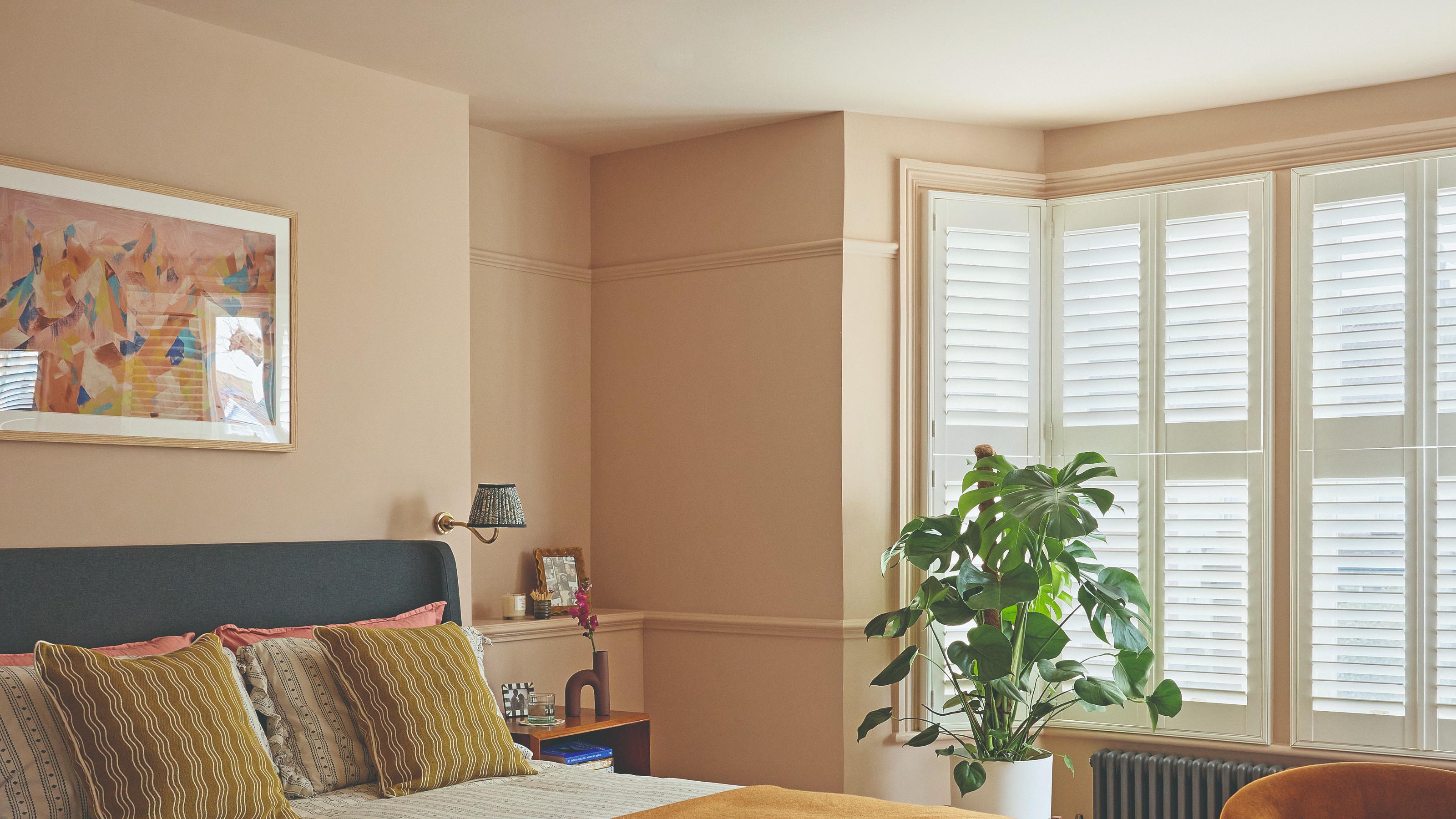 A pink bedroom painted in Little Greene's Masquerade with Masquerade Light on the ceiling and a bed with striped, ruffled bedding