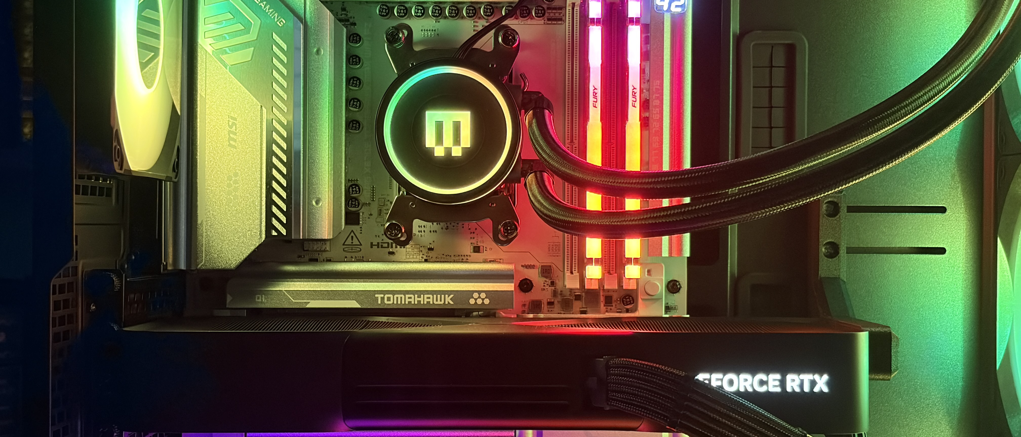 A Maingear MG-1 MK.II gaming PC interior with RGB lighting, featuring a water-cooled CPU, RAM sticks, Tomahawk motherboard, and a GeForce RTX graphics card, conveying a tech-savvy vibe.