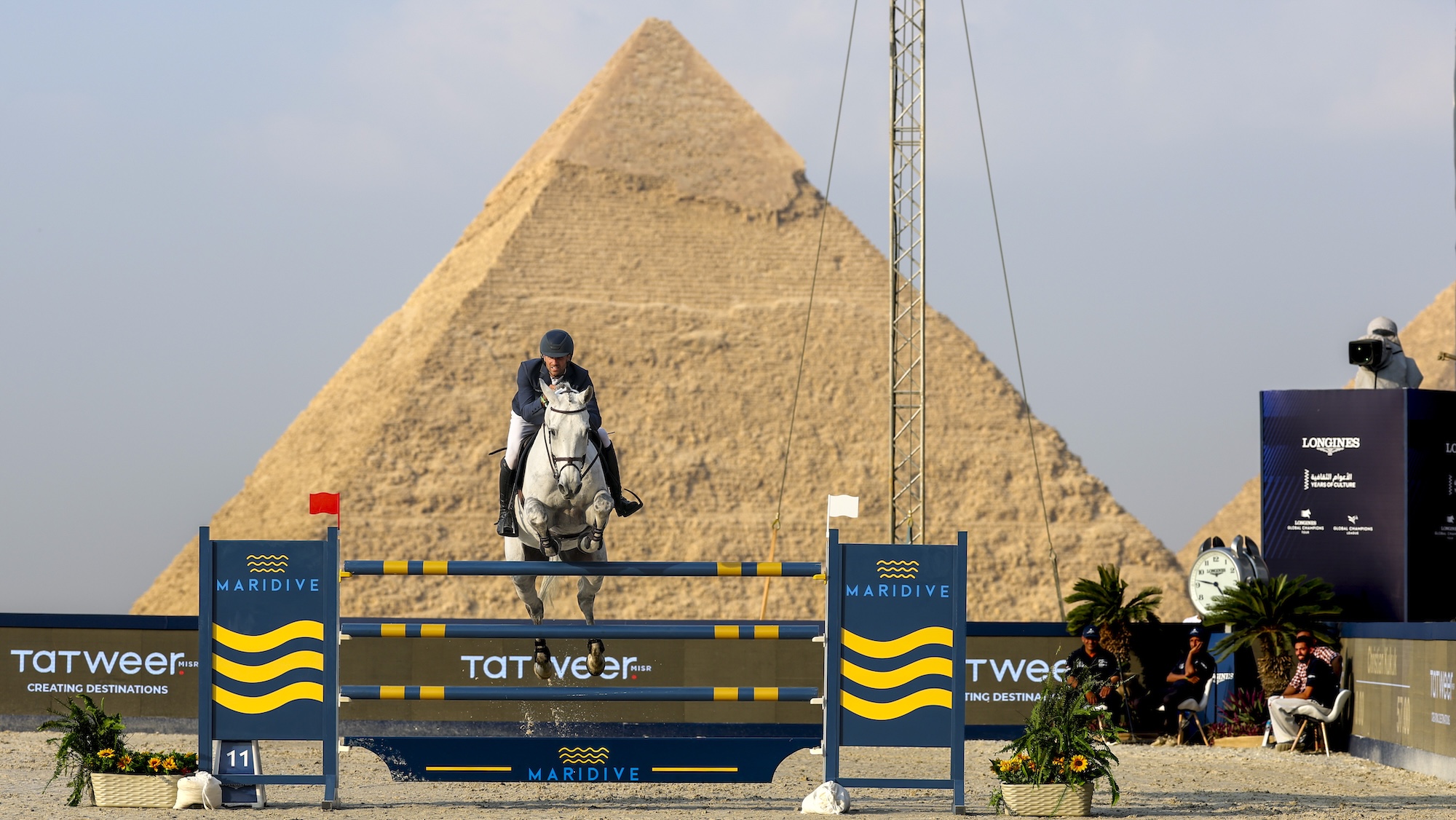 A horse and rider clear a fence with one of the Pyramids in the background