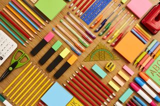 Several coloured pens and pencils are lay on a wooden table.