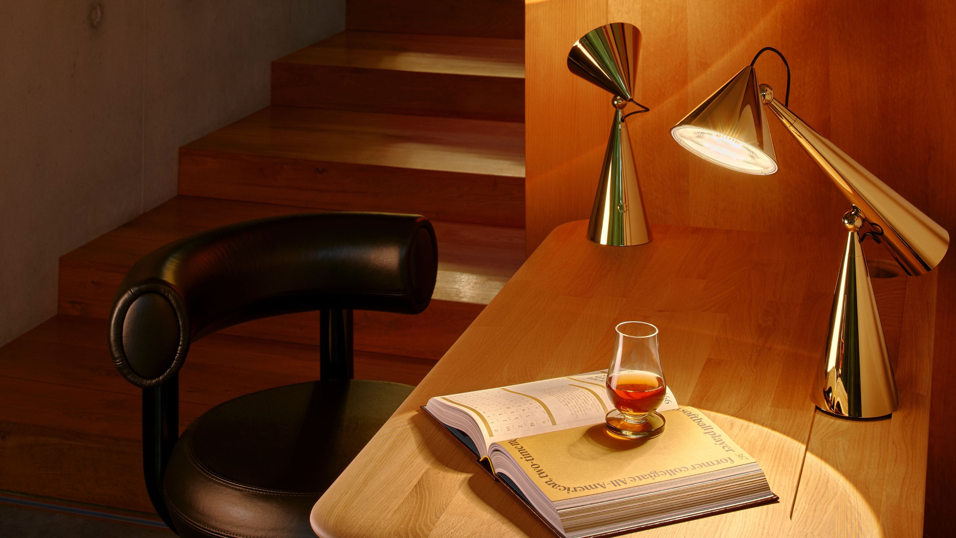 Two POSE Portable lamps on a desk of an office. On the desk is also an open book with a glass on top.