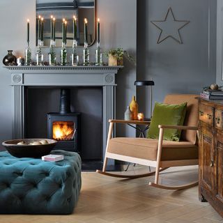 Living room with dark grey walls, a woodburner fireplace, a wooden rocking chair and a green-blue plush button detailed footstool