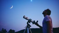 Telescope Deals: Image shows man with telescope against twilight background.