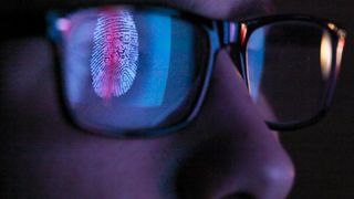 A programmer looks at a screen with a fingerprint reflecting in his glasses
