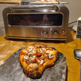 Cooked pizza next to the Sage Smart Oven Pizzaiolo