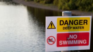 A danger, no swimming sign with a reservoir in the background