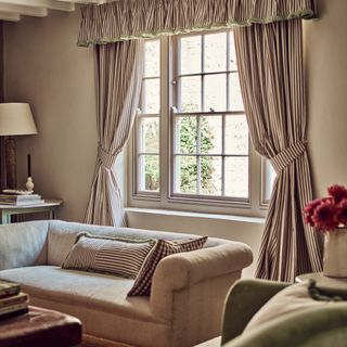 cottagecore decor ideas for living rooms, living room with stripe curtains and pelmet with trim, matching cushion on taupe sofa
