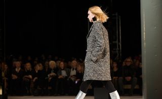 Catwalk model wearing a grey coat, black tights and silver boots