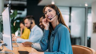 Dark-haired woman using a headset at a desk to support a customer over the phone