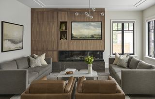 modern living room with TV built into timber cabinetry, with shelves, two gray sofas facing each other and two brown leather armchairs