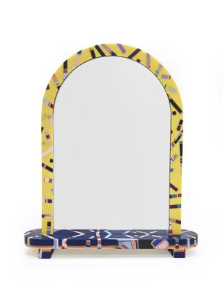 Colourful vanity arch shaped mirror. Arch shape is predominantly yellow with colourful geometric design and the base is predominately blue with colourful geometric design. Photographed against a white background