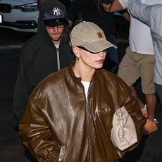 Hailey Bieber wearing a brown leather jacket and baseball cap