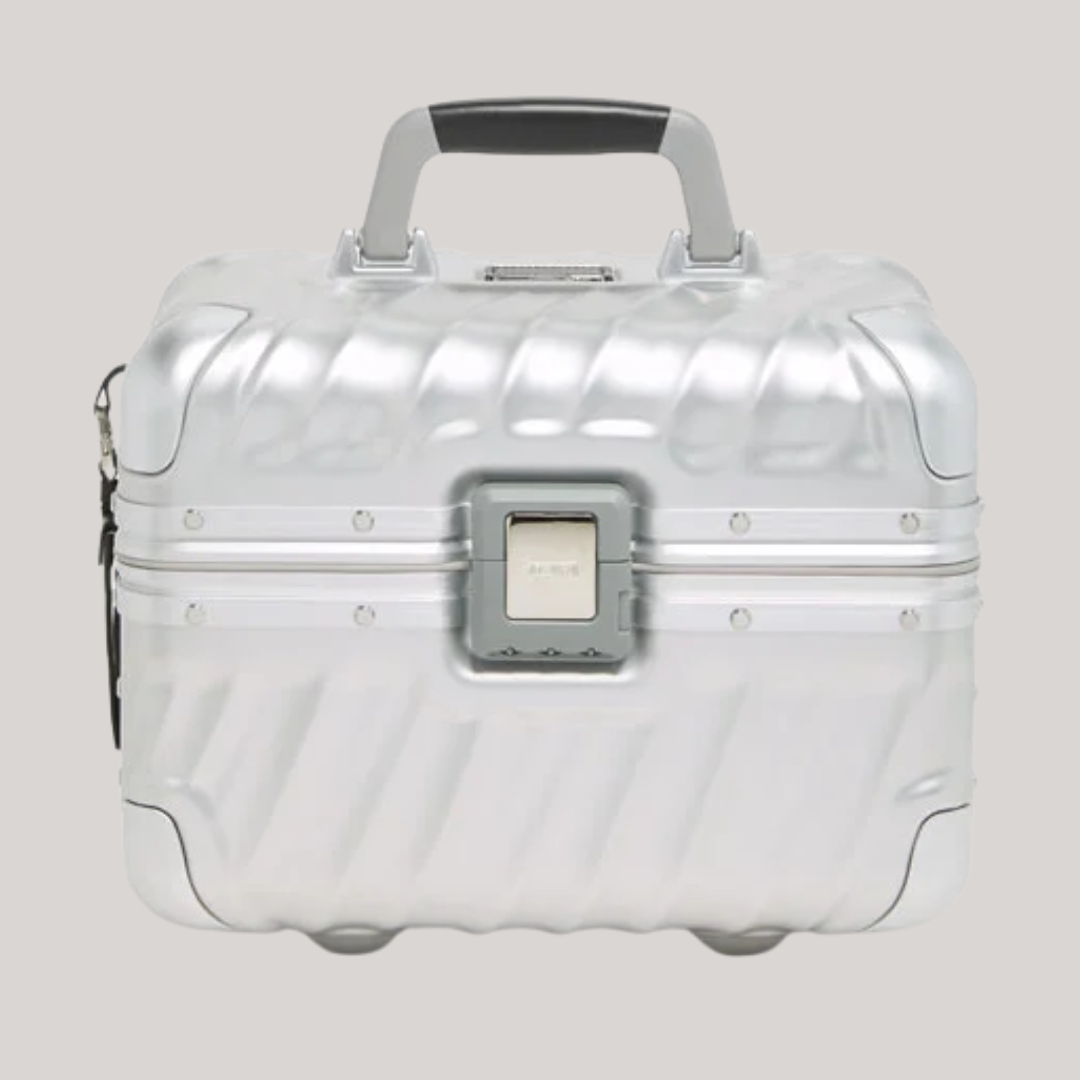 A chrome train case featuring a wavy surface, black and gray handle, and a closure in a slightly darker shade of gray sits against a gray background.