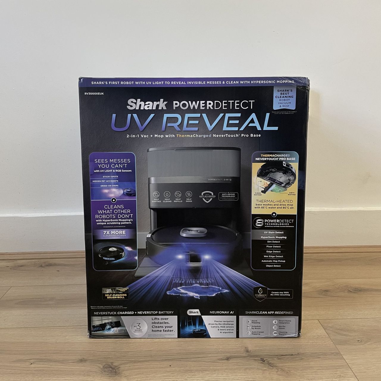 Box of the Shark PowerDetect UV Reveal 2-in-1 Vac &amp; Mop Robot Vacuum sitting on wood-effect flooring in front of a white wall