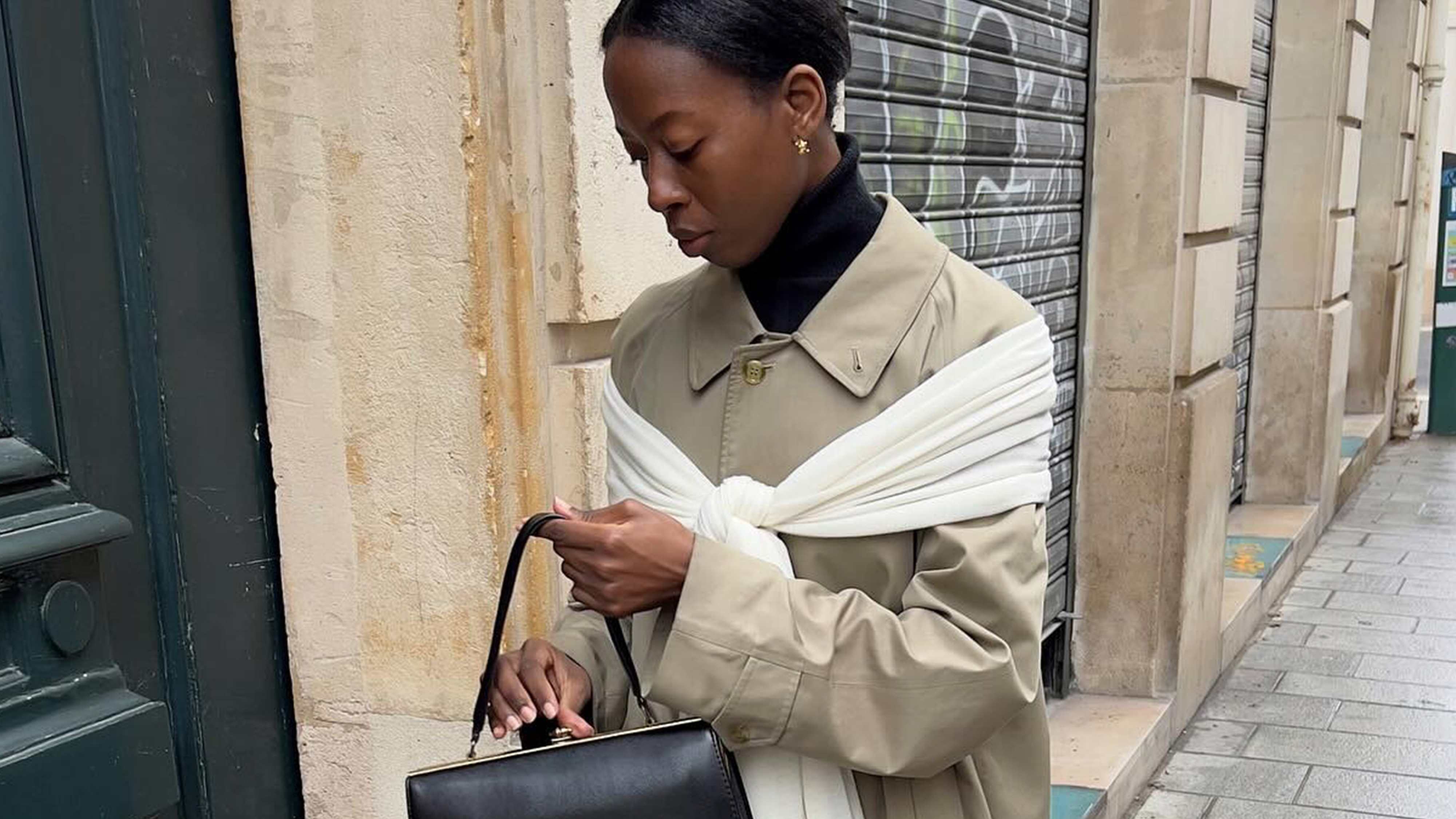 French woman wearing cotton khaki trench coat with white sweater draped across her shoulders.