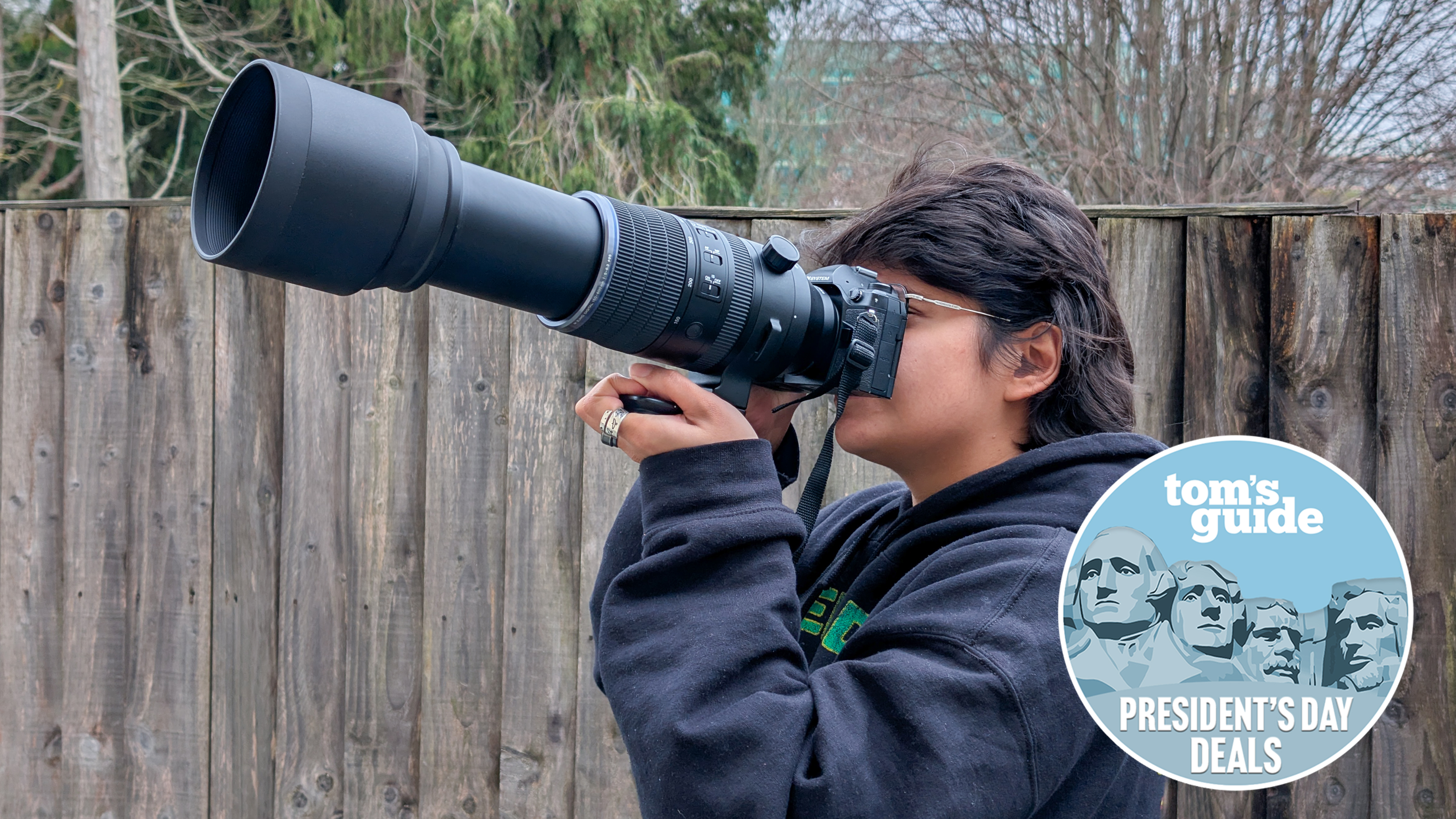 A photo of a person holding an OM System OM-1 Mark II with a 150-600mm telephoto lens