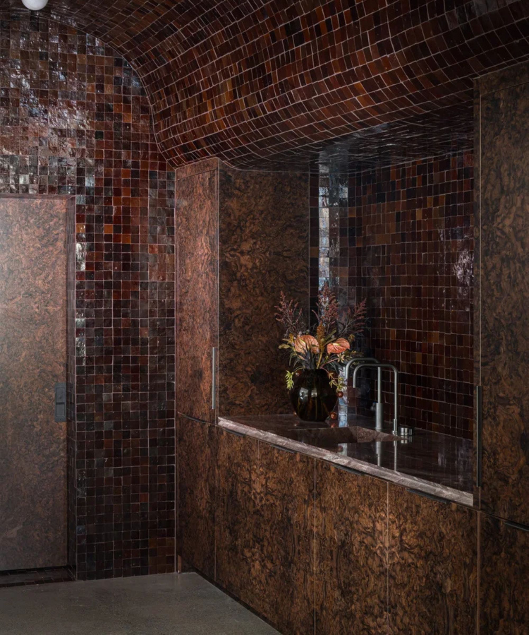 a bar area with burl wood cabinetry, dark brown zellige tile, a sink, and a vase of flowers on the countertop