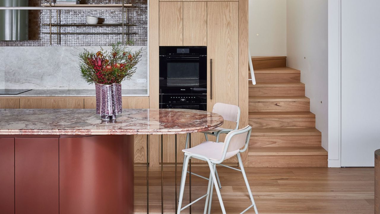 A kitchen with a rounded island made in red marble, and wooden flooring