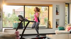 Woman doing indoor walking workouts on treadmill with large glass window in living room