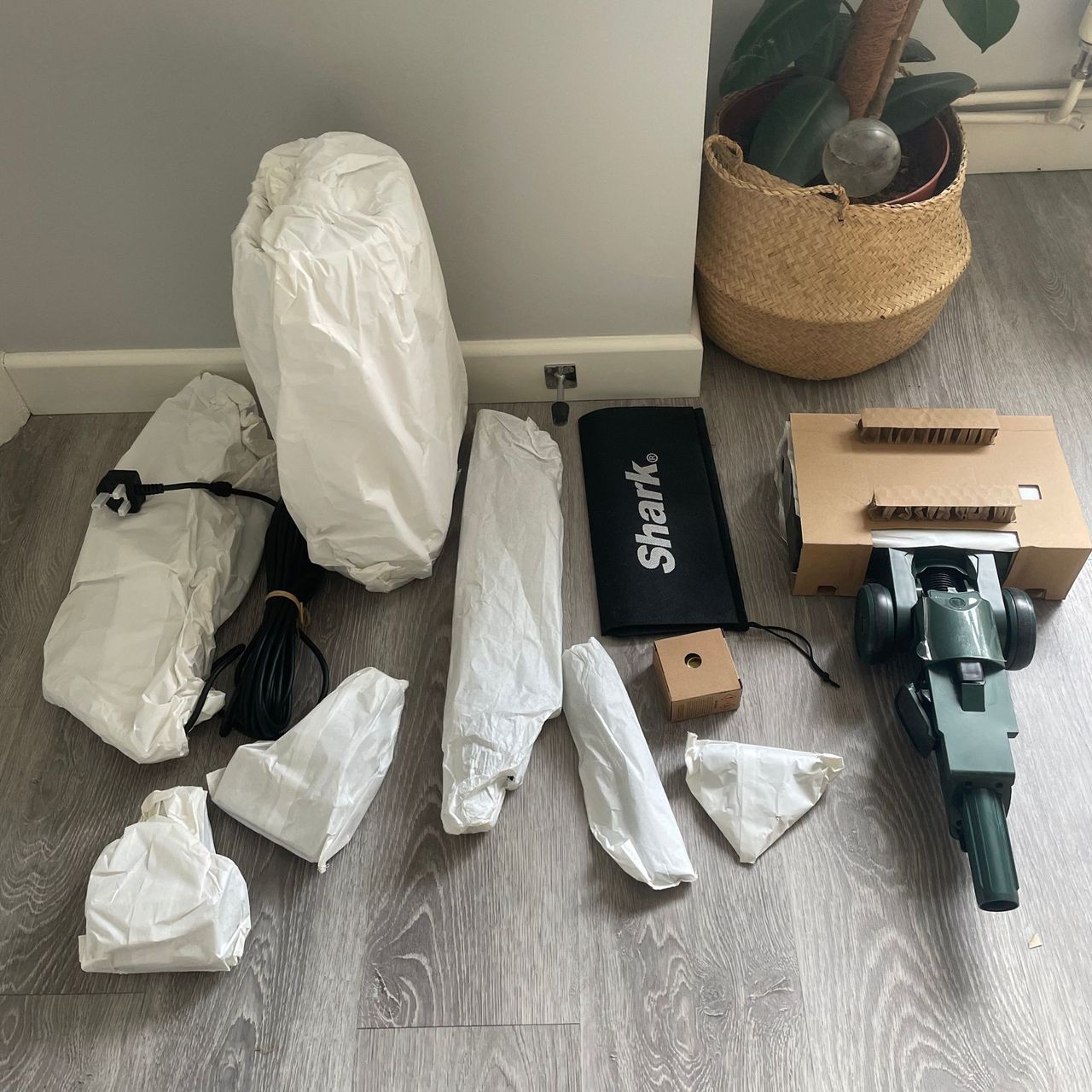 Components of the Shark PowerDetect Transformer Corded Upright Vacuum Cleaner laying on grey floor in their packaging