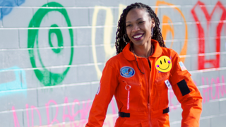 woman in orange jumpsuit in front of a wall with colorful letters 