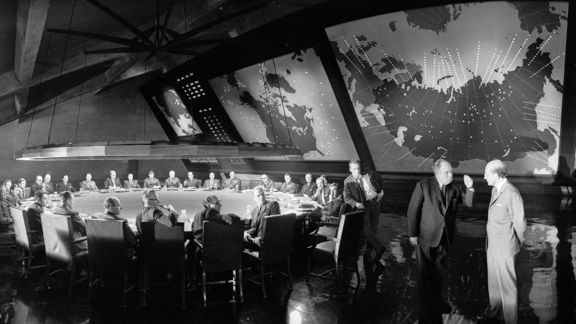 black and white shot of a big war room. there is a circular table encircled by more than 15 people. it's from the movie Dr Strangelove