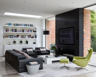 Open plan living space with striking black chimney breast and tv area, large leather sofas and bright green lounge chair with foostool, lots of shelving with books and ornaments, large gray rug with white square coffee table