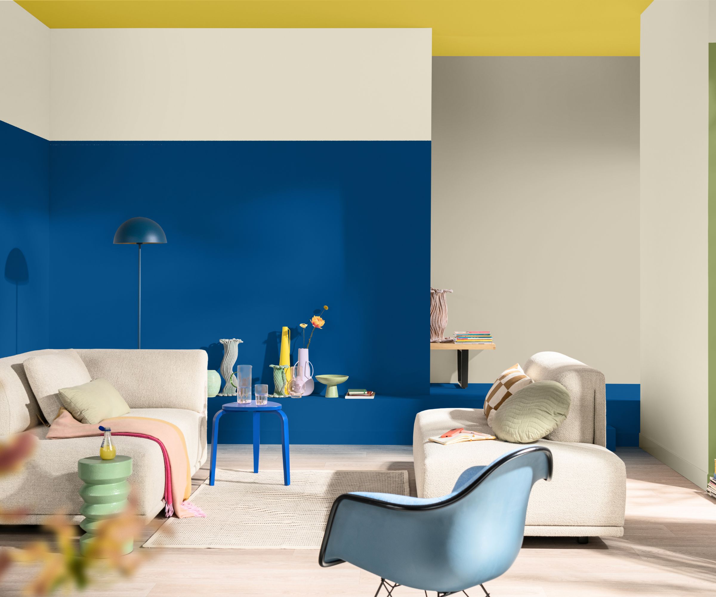 Living room with royal blue painted wall, yellow ceiling, beige sofa, blue armchair and multiple colorful vases
