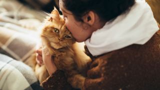 Woman kissing ginger cat on head