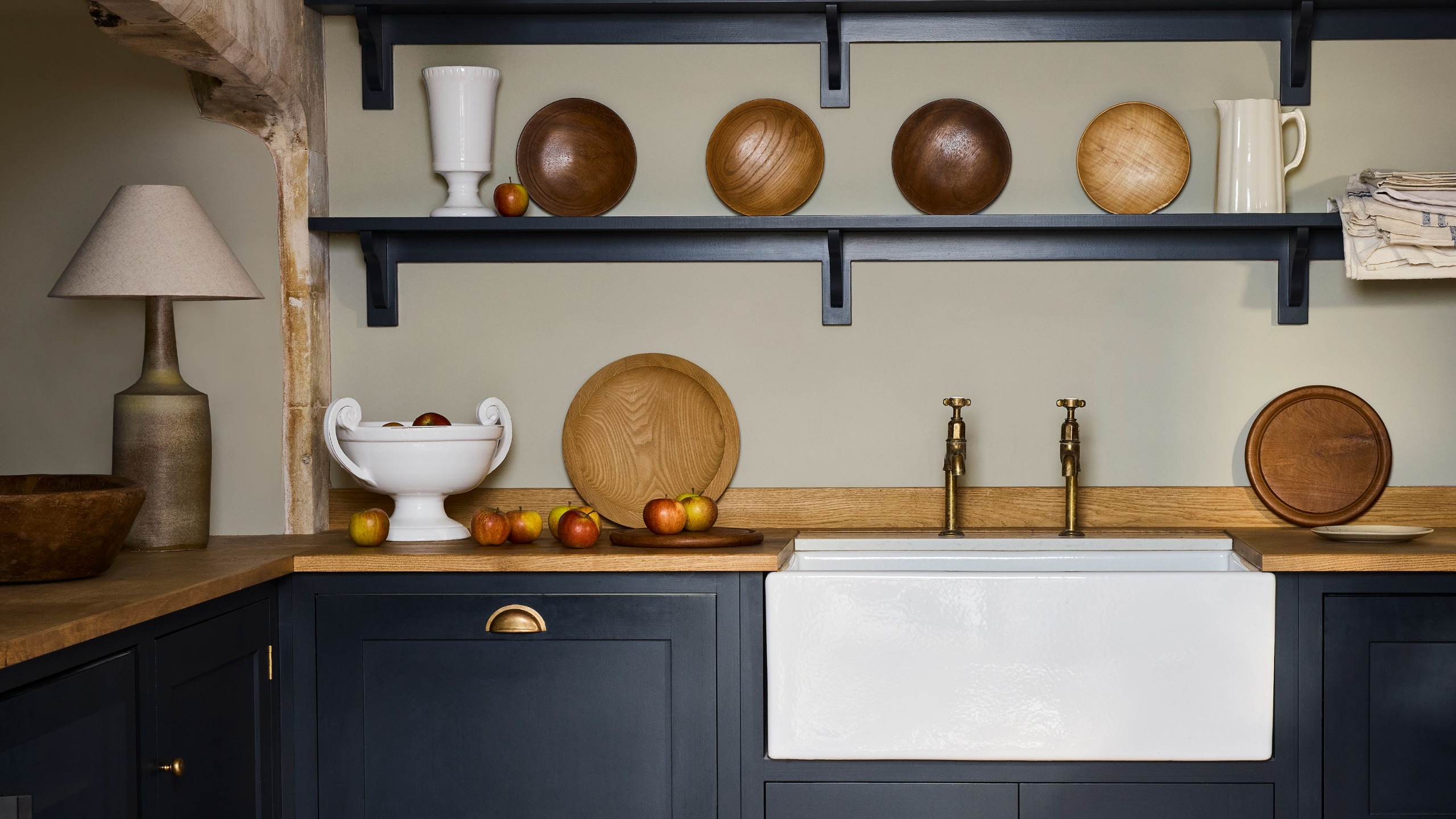 A kitchen with open shelving with the wall painted in Little Greene's new Cobble light grey shade and the cabinets in Basalt,a dark navy blue 