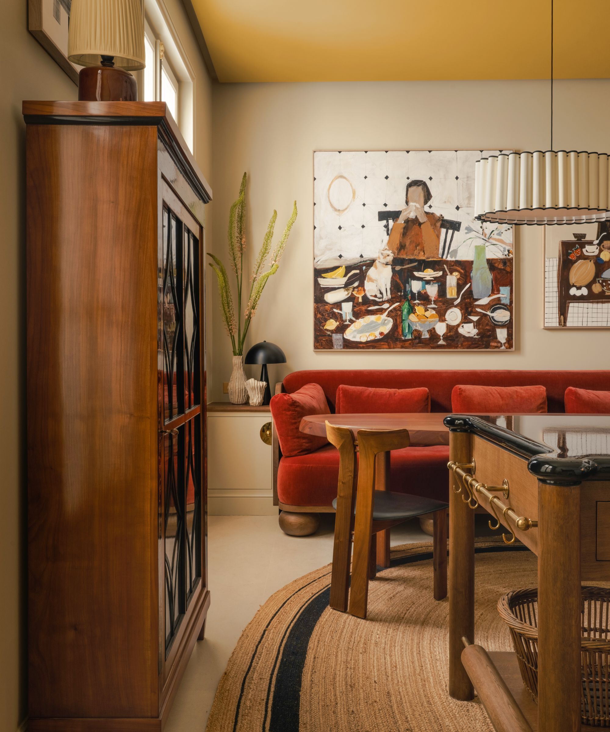 A kitchen with warm white walls, a wooden island and dresser, a red velvet sofa, and a yellow ceiling.
