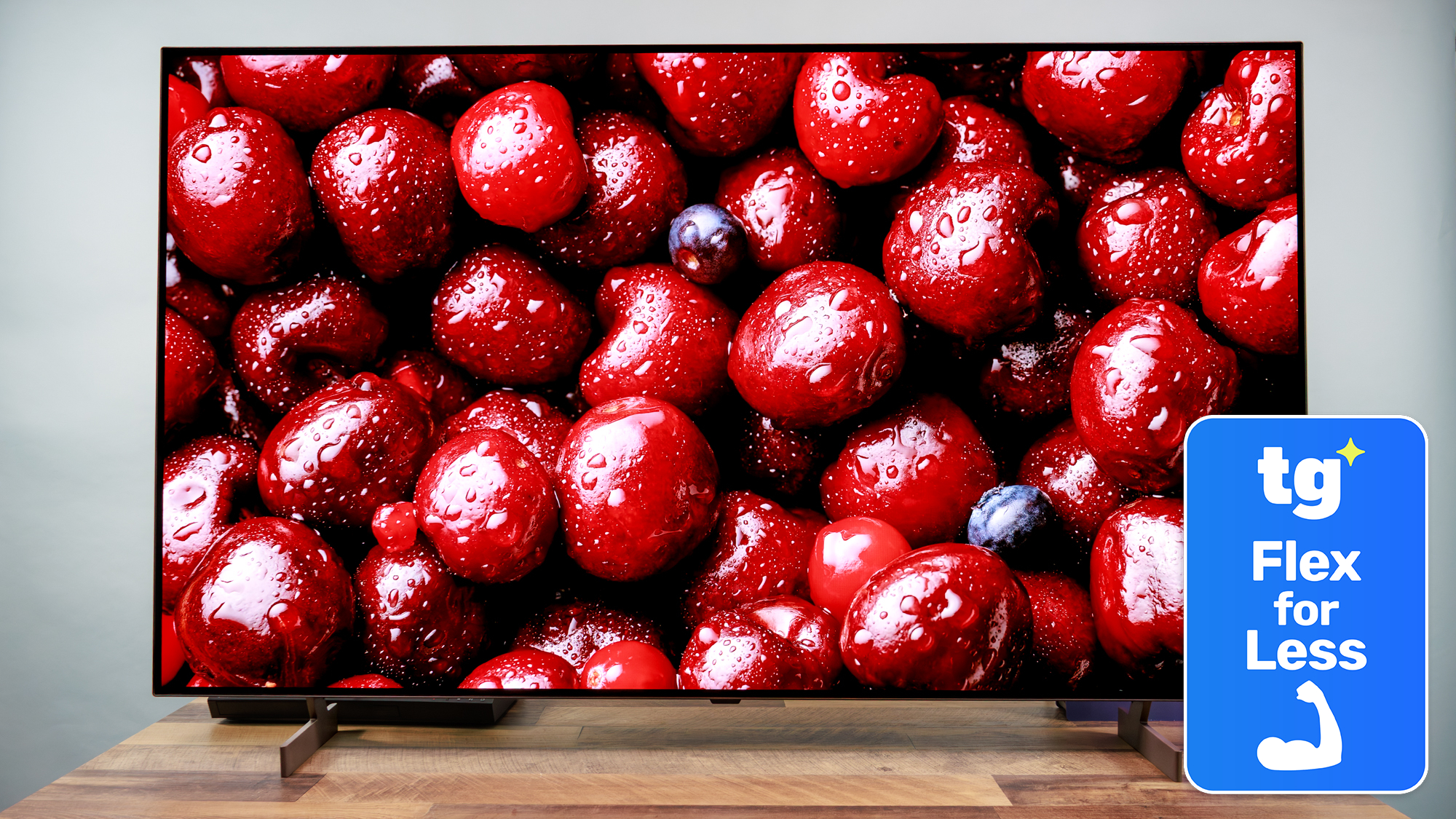 The LG B6 OLED TV displaying a high-contrast, close-up image of dark red-colored cherries. Next to the TV is a superimposed badge that reads: "TG Flex for Less".