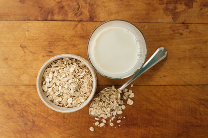 oat milk next to a pot of oats on a wooden table