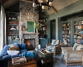 library with exposed stone fireplace wall, green bookcases, dark blue sofa and floral cane chairs