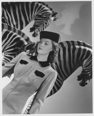 a woman in a suit and bill box hat stands next to three zebras Love Crazy