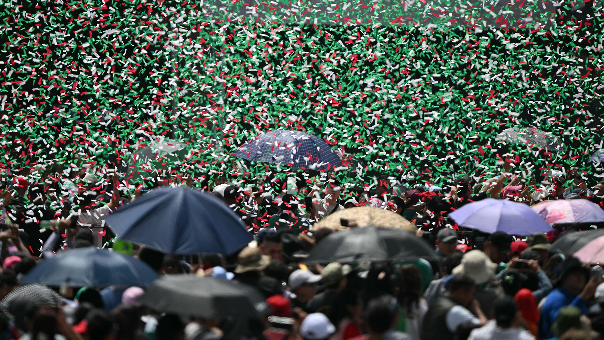 People shelter under umbrellas as red, white and green confetti falls during the Independence Day military parade at Zocalo Square in Mexico City, Mexico