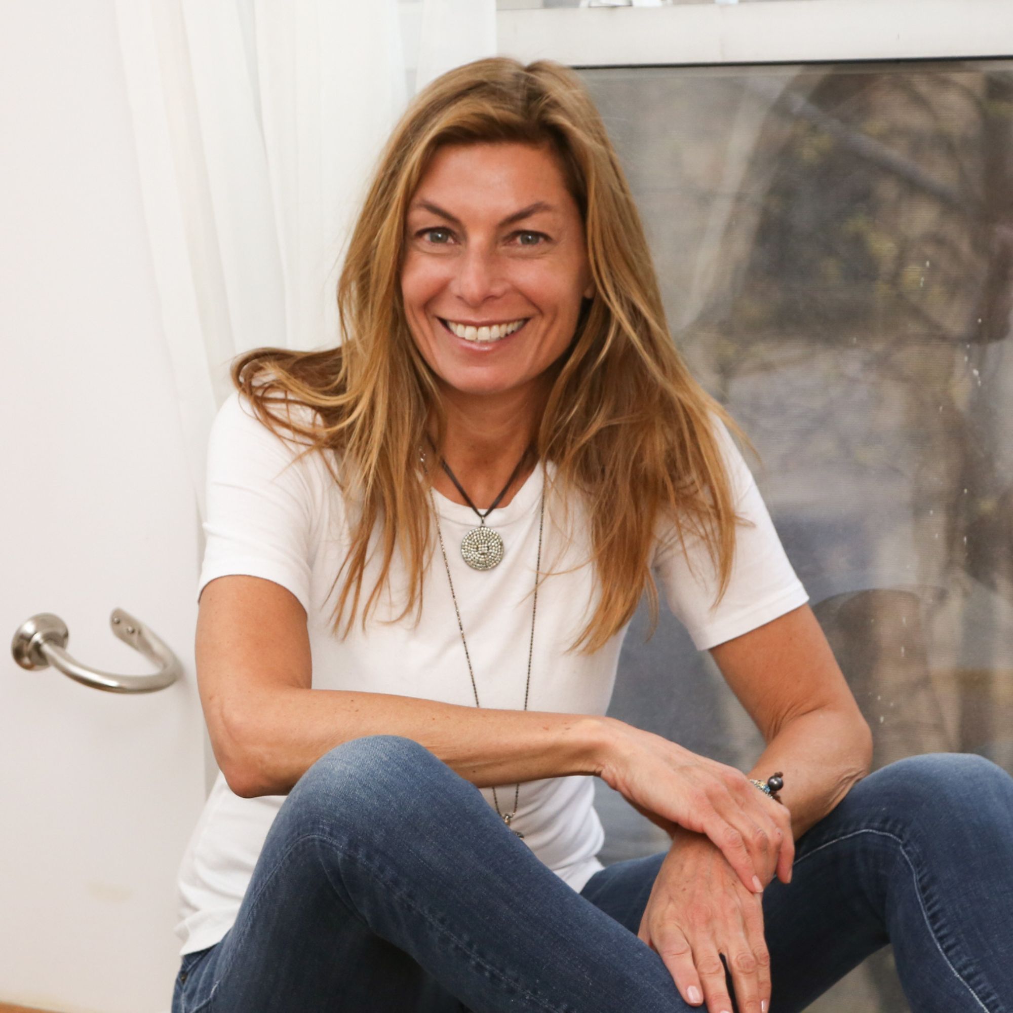 A picture of Hillary Cooper - a woman wearing a white t-shirt and jeans sitting on a windowsill.