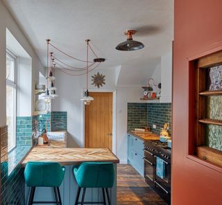blue kitchen with teal/blue wall tiles, wooden floor, hanging pendant lights, L-shape kitchen with island