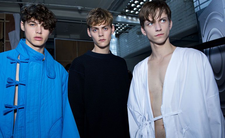 Three guys wearing Craig Green Collection of 2015. The striped quilting and drapes of chemical blue cotton, as well as the ties and sashes are indicative of this collection.